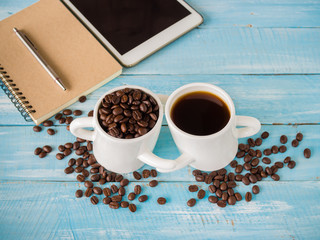 Two cup of hot coffee and roast seeds coffee  on wooden background.