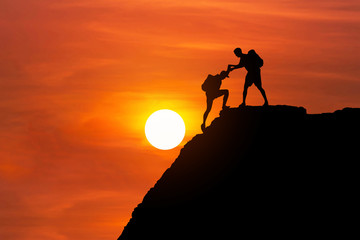 silhouette mountaineer gives helping hand his friend to climb high cliff mountain together. teamwork success concept.