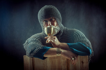 Powerful bearded knight with the glass of wine on the dark background.