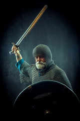 Powerful bearded knight with the sword and shield on the dark background
