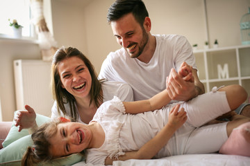 Fototapeta premium Parents having fun with their little daughter on bed. Family spending time at the morning.