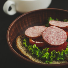 A sandwich: bread, a leaf of lettuce, paddy and sausage. Black background.