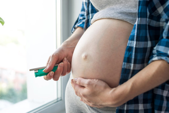 Pregnant Woman Belly Holding A Cigarette And A Lighter. Concept Of Smoking And Bad Habits During Pregnancy