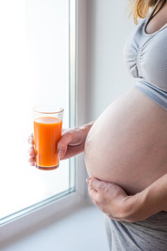 Pregnant woman with belly holding a glass of carrot juice in hand. Concept for weight control and healthy eating