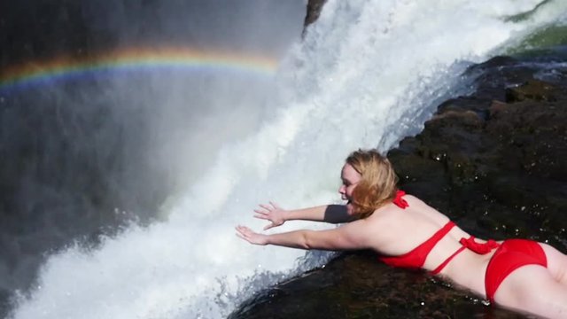 Slow motion, blonde, woman lays on waterfall
