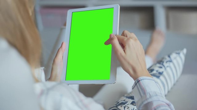 Young Woman in white jeans laying on couch uses Tablet PC with pre-keyed green screen. Few types of gestures - scrolling up and down, tapping, zoom in and out. Perfect for screen compositing