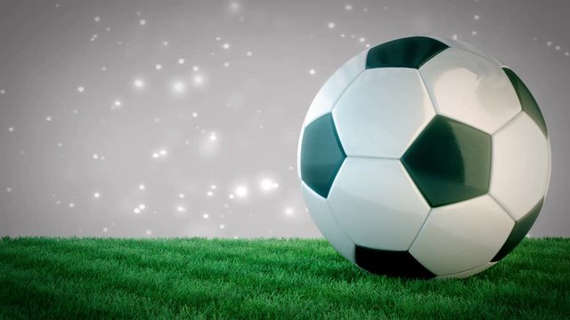 Rotating glossy soccer ball on grass field with bokeh background - seamless loop
