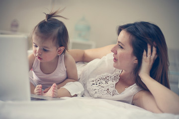 Mother and her little baby at home. Mother with her baby watching something on laptop.