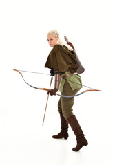 full length portrait of a blonde girl wearing green and brown medieval costume, holding a bow and arrow. isolated on white background.