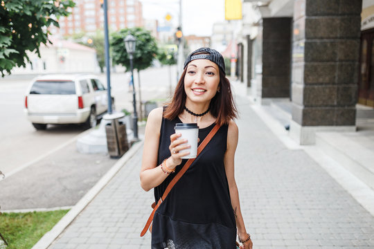 An independent young woman strolls through the streets of the city with a disposable cup of coffee in her hand