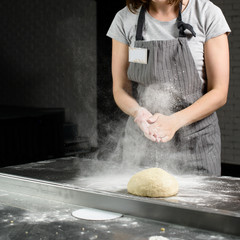 woman baker sprinkled flour on roll dough on a wooden board. Process of preparing pizza. Cooking...