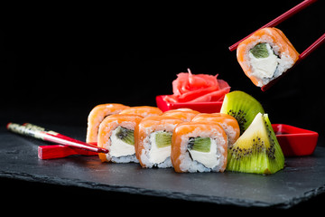 traditional Japanese cuisine. Process of eating sushi rolls with salmon, cream cheese, rice and kiwi on dark background, selective focus