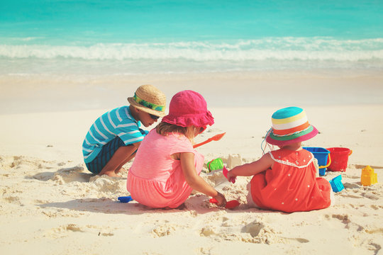 little girls and boy play with sand on beach