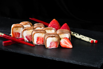 new trend in the Japanese cuisiune. Sweet sushi rolls in pancake with cream cheese, strawberry and banana on dark background