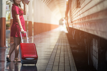 Fototapeta na wymiar Woman with suitcase waiting for her train on platform of railway station