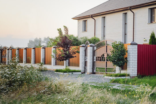 A brown fence made of polyprofile with a canopy in a modern style with brick columns, the design of a country house.