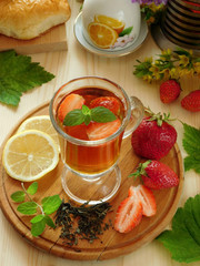 Spicy tea with strawberries illuminated by the sun rays on a wooden background