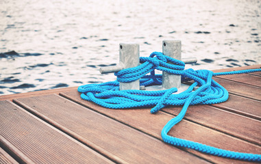 Cleat with blue rope on a wooden pier, travel or safety concept, color toning applied.