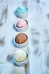 Selection of gourmet flavours of Italian ice cream in vibrant colors served in individual porcelain cups on an old rustic wooden table in an ice cream parlor, angle view jpg