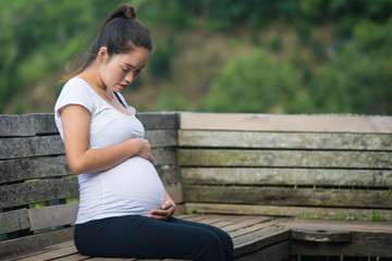 Young beautiful pregnant woman hands holding belly and sitting on wooden chair at mountain.
