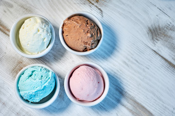 Selection of gourmet flavours of Italian ice cream in vibrant colors served in individual porcelain cups on an old rustic wooden table in an ice cream parlor, angle view jpg