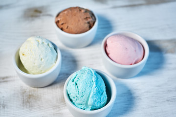 Selection of gourmet flavours of Italian ice cream in vibrant colors served in individual porcelain cups on an old rustic wooden table in an ice cream parlor, angle view jpg