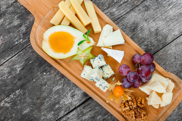 Fototapeta na wymiar Cheese platter garnished with pear, honey, walnuts, grapes, carambola, physalis on cutting board on wooden background. Snacks and Wine appetizers set. Top view
