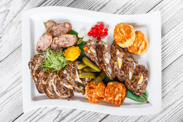 Juicy delicious meat cutlets and homemade sausage with pickled vegetables on plate on wooden background. Meat appetizer. Top view