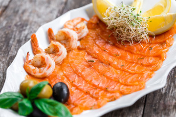 Seafood platter with salmon slice and shrimp, decorated with olives and lemon on wooden background close up. Mediterranean appetizers. Top view