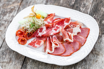 Antipasto platter cold meat plate with prosciutto, slices ham, salami, decorated with physalis and slices of melon on wooden background. Meat appetizer. Top view