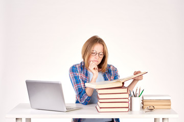 Beautiful teenage schoolgirl sitting at desk with stack of books on it