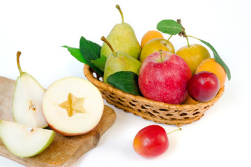 Fruit composition - a wooden wicker basket with whole ripe fruits - pears, plums, apricots and apples, near the sliced apple and pear on a wooden board. White background.