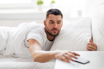 young man reaching for smartphone in bed