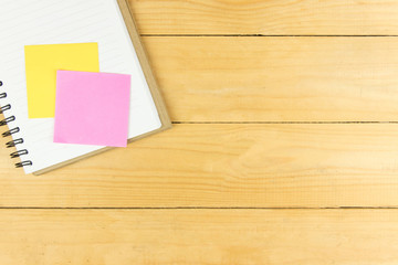 Pink and yellow post it on blank notepad on wooden table
