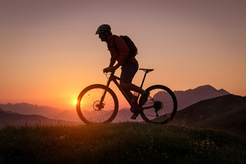 Obraz premium Silhouette of a male mountainbiker at sunset in the mountains