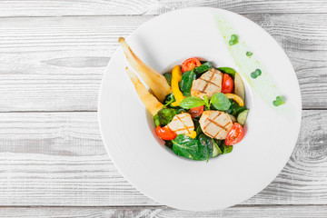 Fresh salad with chicken breast, baby spinach, basil, cherry tomatoes, pear, cucumber on plate on wooden background close up. Top view