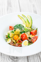 Fresh salad with tuna, spinach, arugula, codfish, artichokes, quail eggs, avocado, cherry tomatoes, physalis and sesame on wooden background close up. Mediterranean food