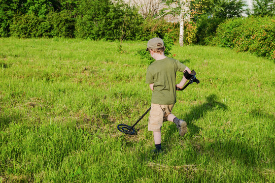 boy with a metal detector on a green meadow