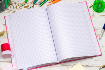 Outdoor notebook surrounded by school supplies on a white wooden background with empty space for inscriptions.