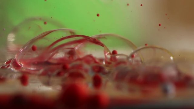 Group of red bubbles pop on water, slow motion