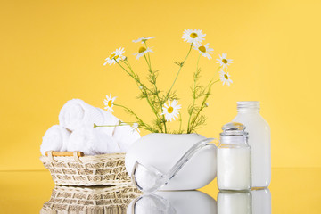 Spa. Chamomile in a vase, white towels, jars of cream, a spoon with sea salt on a yellow background