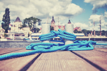 Color toned picture of a cleat with blue rope on a wooden pier, Szczecin waterfront in distance, Poland. - obrazy, fototapety, plakaty