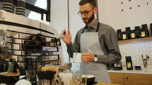 Portrait of attractive barista in the glasses preparing cup of coffee for customer in modern coffee shop. View from the side.