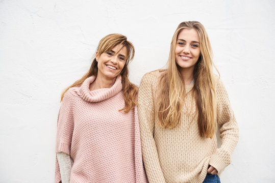 Mother and daughter standing against white wall