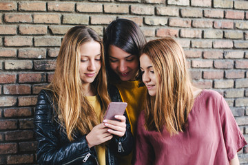Teen friends looking their smartphone in front of a brick wall.