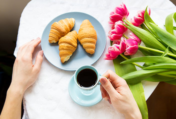Girl with croissants and coffee, a bouquet of pink tulips, happy morning.