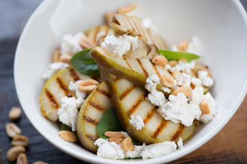 Close-up of salad with grilled pear slices, fresh spinach leaves, cheese and nuts, selective focus, horizontal shot