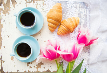 Fototapeta na wymiar nice cup of coffee, croissants and pink tulips on old white table.