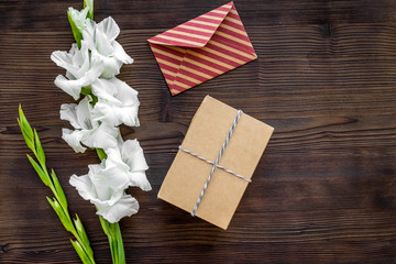 Fototapeta na wymiar Congratulation. Envelope and box in kraft paper near flower gladiolus on wooden table top view copyspace