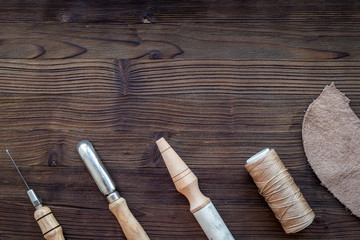 Leather craft. Knife, awl and other tools on dark wooden background top view copyspace